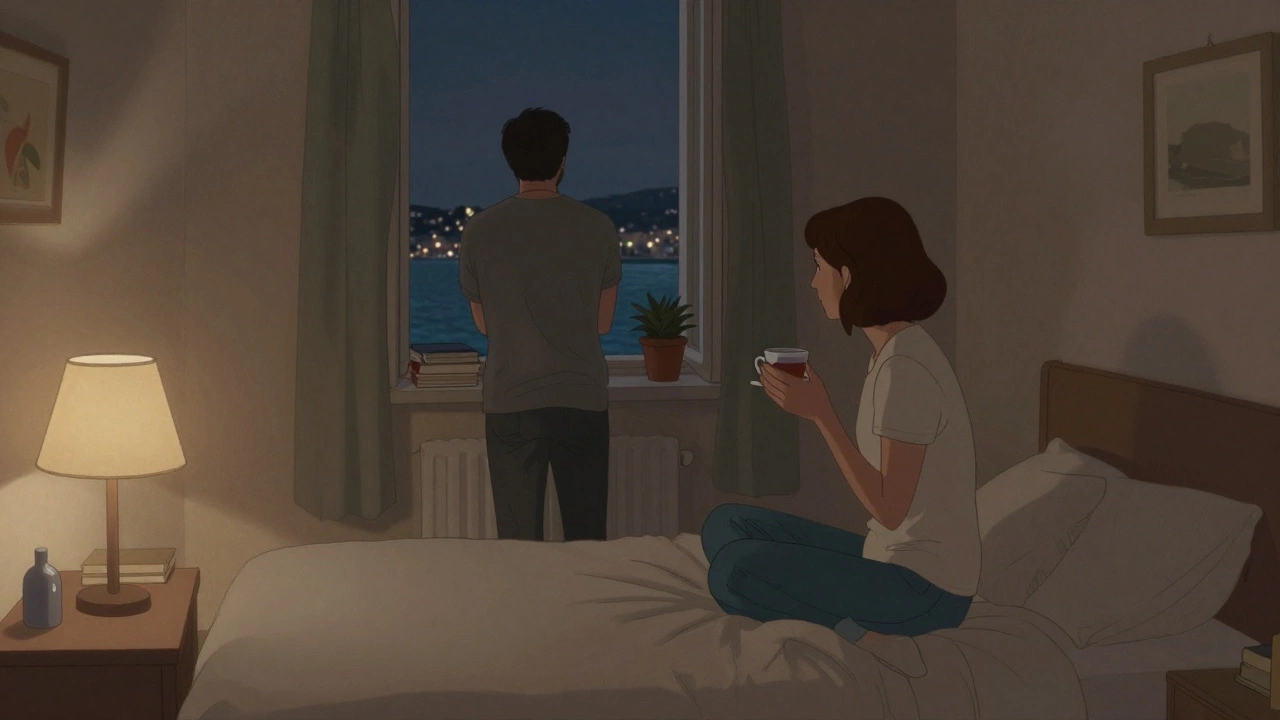 A woman sits on a bed in a quiet Toulon apartment, sipping tea as light from the harbor glows through the window.